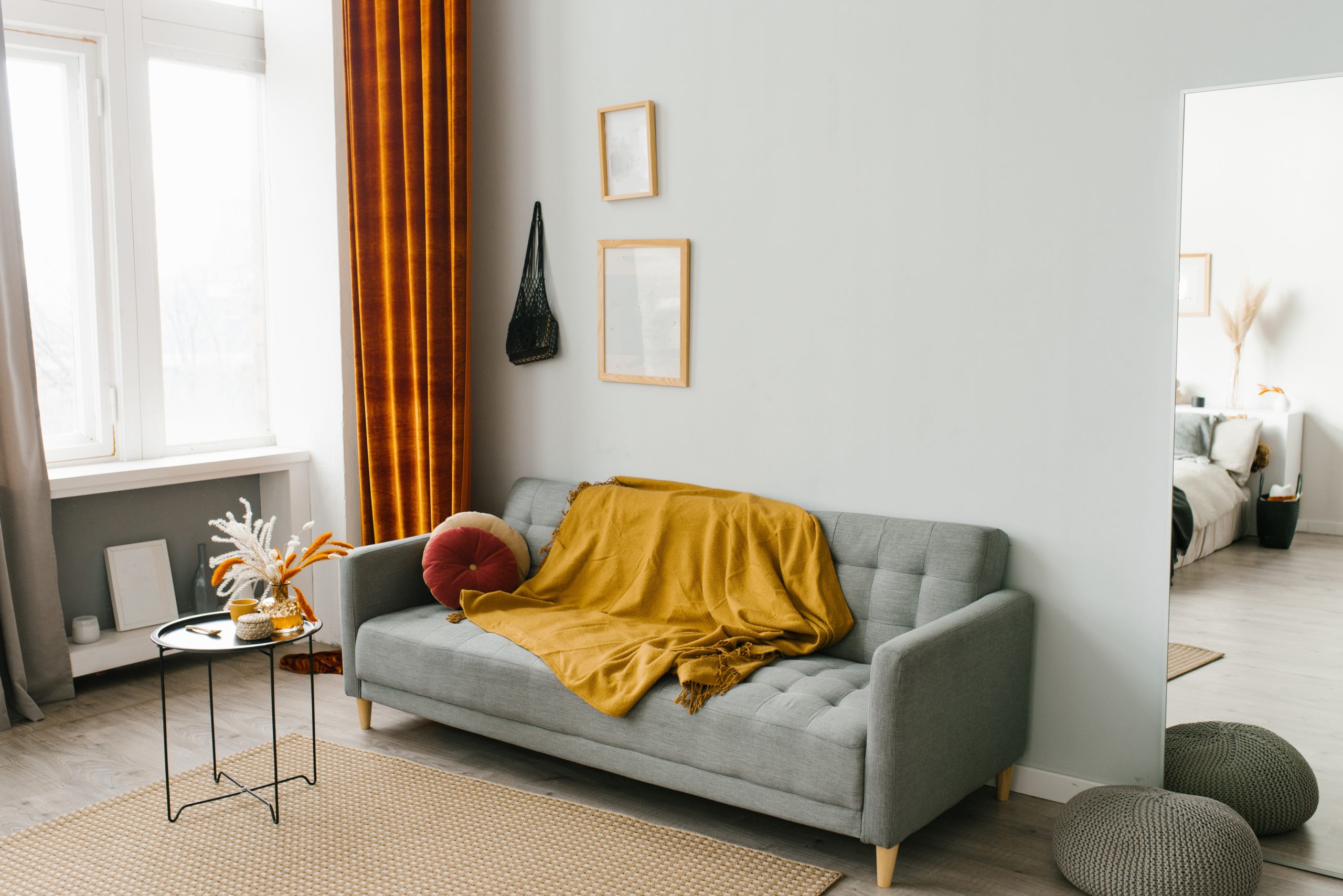 The interior of the living room in a Scandinavian minimalist style in gray-yellow-orange colors: sofa, coffee table, mirror.